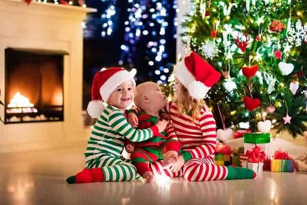 Happy little kids in matching red and green striped pajamas decorate Christmas tree in beautiful living room with traditional fire place. Children opening presents on Xmas eve.