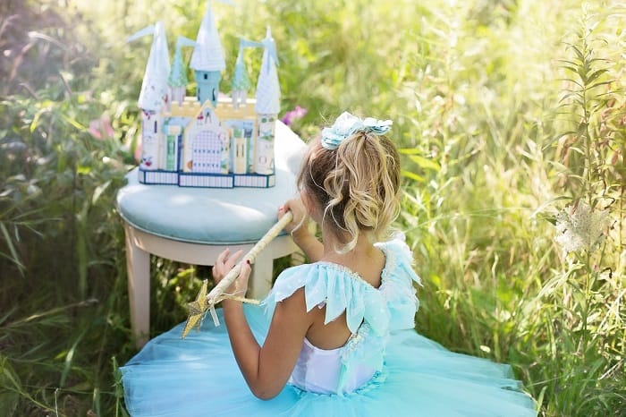 Little girl dressed up as princess sitting in front of a play castle