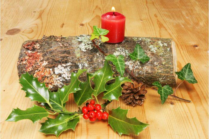 A wooden log decorated with holly leaves, acorns and a red candle.